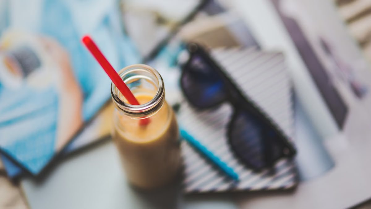 A refreshing smoothie with red straw on an artistic desk setup featuring sunglasses and stationery.